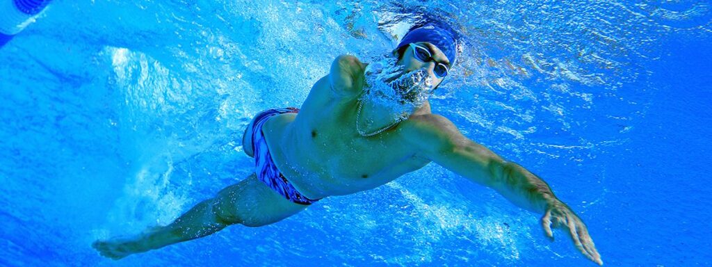 Nageur en situation de handicap effectuant un crawl sous l’eau dans une piscine, symbolisant la performance en handisport